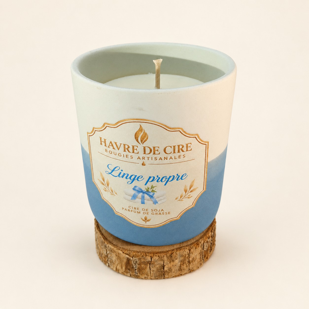 Bougie Havre de Cire Linge propre en cire de soja, pot en céramique blanc et bleu posé sur un rondin de bois, sur fond crème