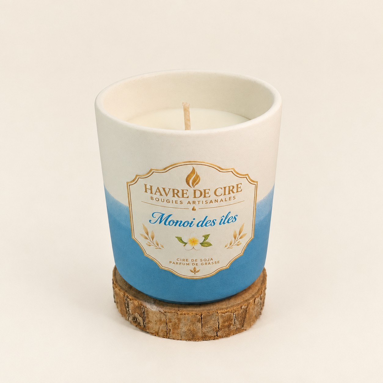 Bougie Havre de Cire Monoï des îles en cire de soja, pot en céramique blanc et bleu posé sur un rondin de bois, sur fond crème